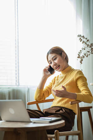 Happy smiling Asian woman relaxing using smartphone to talk and laptop computer in bedroom at home....