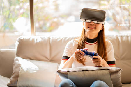 Asian woman using vr glasses, 3D virtual reality headset on SOPA, virtual reality concept, simulation, gaming and technology of the future. Asian women playing games in the roomの写真素材