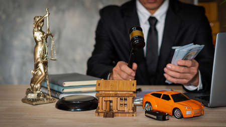 Close-up of the house in front of a lawyer holding hammer and money with the laptop, brass scales, car on wooden table in the law office, legal services, advice, justice, and realの写真素材