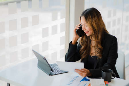 Freelance Asian woman working on smartphones and tablet computers in a modern office. make an...