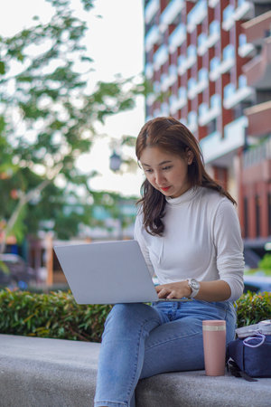 Beautiful schoolgirl learning with laptop computer while sitting on the floor outdoors, online...
