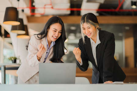 Two young Asian women celebrating success or happy poses with laptops. Working together. Diversity....