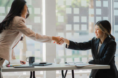 Asian women and interviewees shake hands. Businessman shaking his colleague's hand during a meeting with colleagues around a table in an office conference room. greeting agreementの写真素材