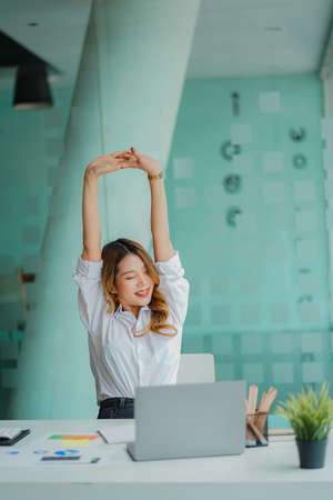 Asian businesswoman relaxing during office work with financial graph on laptop computer desk financial accounting conceptの写真素材