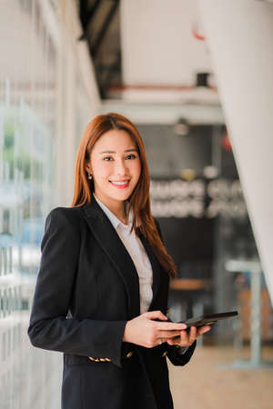 Freelance Asian woman working on a computer tablet in a modern office. make an account analysis report on real estate investment information financial system concept and tax verticの写真素材