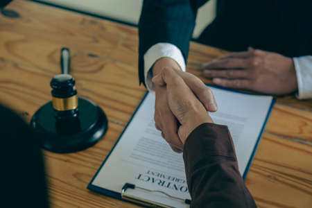 Businessmen shake hands after consulting the law from lawyers, judges, and legal counsel. Consulting services on various contracts to plan a court case with hammers and scales nextの写真素材