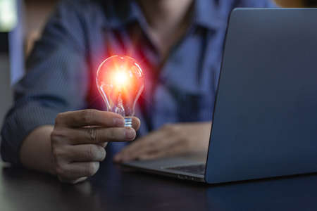 energy saving concept businessman holding a light bulb on a laptop with bright light