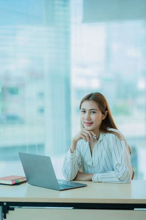 Beautiful ambitious Asian female employee working from home. girl using laptop smile like a dream Students feel inspired to write an essay.の写真素材