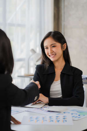 Two smiling female business partners shaking hands in the office teamwork office girl to make a deal in a meeting to discuss financial graph and laptop computerの写真素材