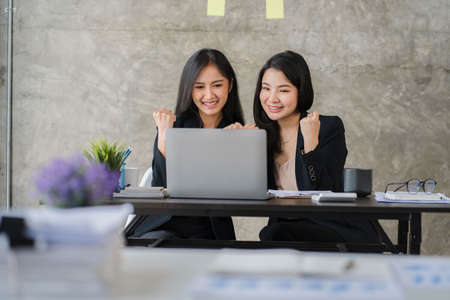 Two Asian business women working on laptop computers. holding a pen and looking at the screen in the office teamwork and customer care concept online meetingの写真素材