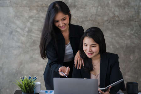 Two Asian business women working on laptop computers. holding a pen and looking at the screen in the...
