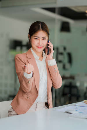 Asian businesswoman holding a smartphone working on project statistics on device Presentation with graphs and an entrepreneur's accountant laptop analyzing financial data. show chaの写真素材