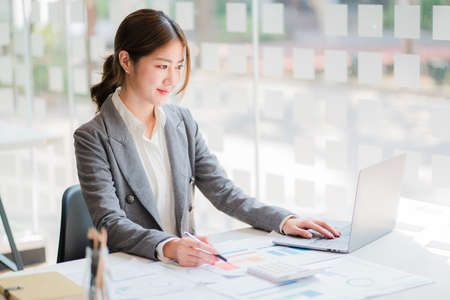 Attractive and professional Asian businesswoman working in the office. Using a laptop computer to analyze financial data, charts using a calculator with documents and holding a penの写真素材