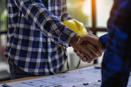 Architect engineers shake hands with hats and houses on construction tool tables. with blueprints on the table - business teamwork working together Successful Collaboration Ideasの写真素材