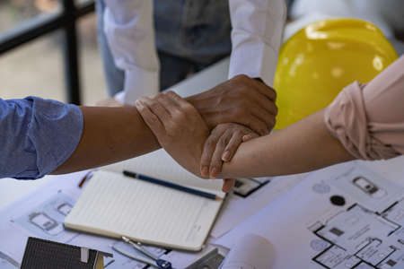 Architect engineers shake hands with hats and houses on construction tool tables. with blueprints on...