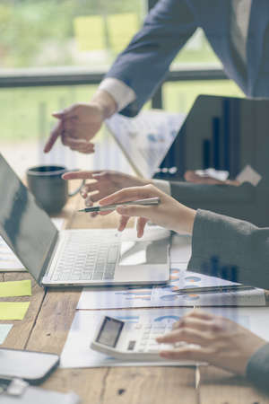 Business team meeting, teamwork concept of business merger at the office. A variety of colleagues work using graphs and computers sitting at their desks in the office. vertical picの写真素材