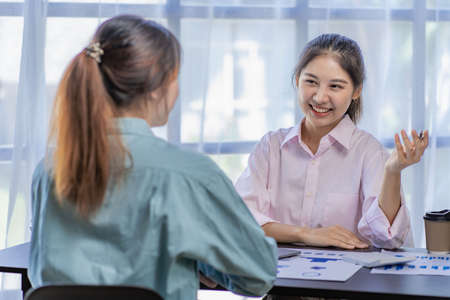 Starting a business, two young Asian women discuss working on investment projects and planning strategies. Businessman talking with laptop computer at officeの写真素材