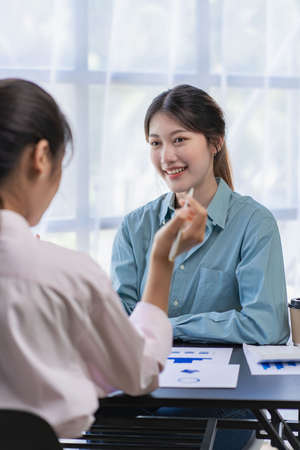 Starting a business, two young Asian women discuss working on investment projects and planning strategies. Businessman talking with laptop computer at officeの写真素材