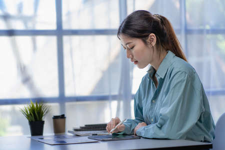 A young Asian female accountant or manager sits at her desk. Reading and reviewing account sales in reportsの写真素材
