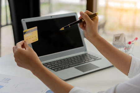 Close-up photo. Asian businesswoman holding credit card and using laptop computer smart phone to...