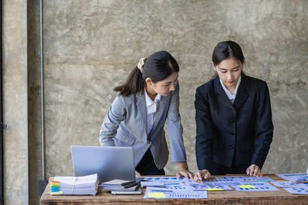 Two young Asian accountants discuss working on investment projects and strategic planning using their office laptops. vertical pictureの写真素材