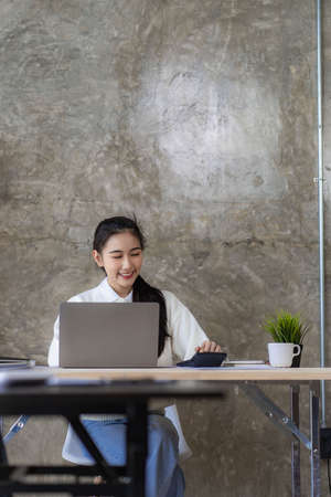 Online study using internet and technology Asian woman using laptop computer to work and study finance with graphs at home.の写真素材