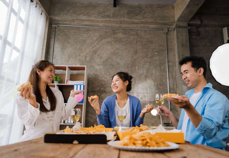 Young Asian male and female colleagues having lunch in the office eating pizza and communicating. The crew of young colleagues are having a pizza party together enjoying their freeの写真素材