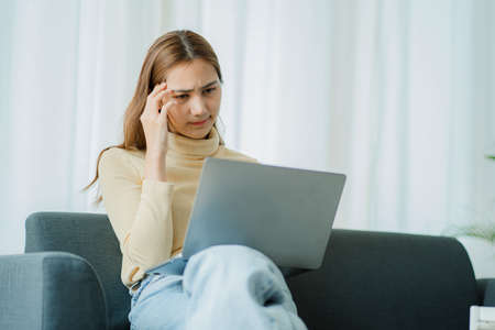 Asian woman doing stressful poses sitting on the sofa working with a laptop on the sofa