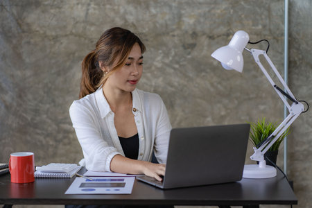 Asian business woman Use a laptop computer and work with the calculator documents on the desk. plan to analyze financial reports Invest in an office business planの写真素材