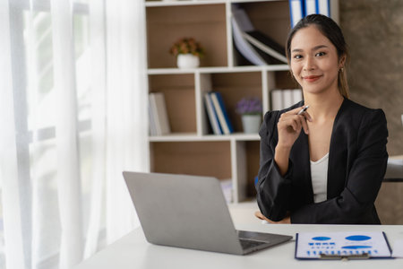 Asian business woman Use a laptop computer and work with the calculator documents on the desk. plan to analyze financial reports Invest in an office business planの写真素材
