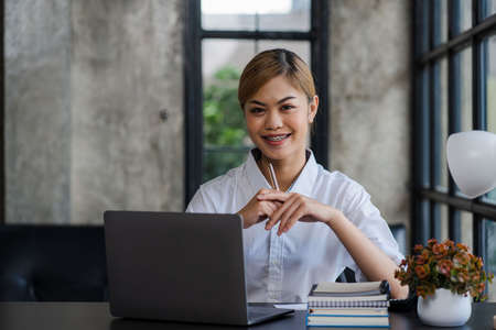 Successful beautiful Asian woman smiling with laptop sitting at home desk at home online learning...