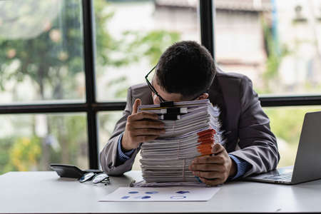 Businessman stressed with work with piles of unresolved documents on desk in officeの写真素材