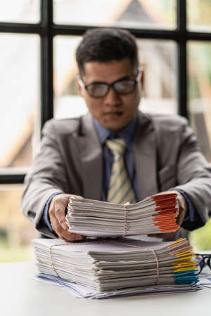 Businessman working piles of paper files to search for information on his desk at home ready. computer keyboard Work in piles of paperwork and unfinished paperworkの素材 [FY310190602028]