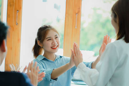 Attractive young businessman and young Asian woman celebrating successful business raising hands at...
