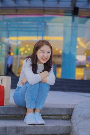 Cute Asian girl sitting in front of the mall with shopping bags. Name concept.の写真素材