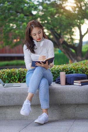Young Asian college student with tiger skin and laptop sitting on the outdoor floor online learning concept outdoorの写真素材