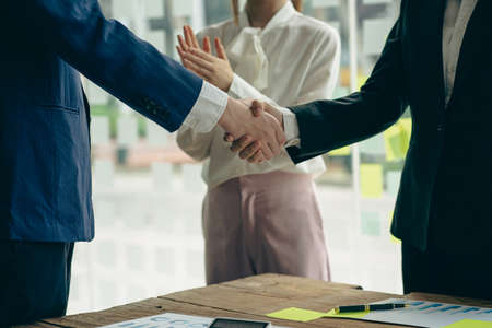 Young businessmen shake hands after a short job to sign a co-working business contract in a modern office with vintage-style images of colleagues at a teamwork meeting.の写真素材