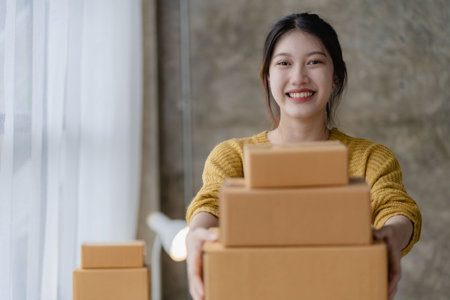 Asian woman working at home with yellow box and laptop for taking orders, sme business ideas on parcel deliveryの写真素材