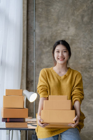 Asian woman working at home with yellow box and laptop for taking orders, sme business ideas on parcel deliveryの写真素材