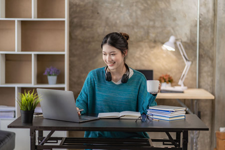 Smiling Asian woman using headset looking at laptop screen listen and learn online courses with a...