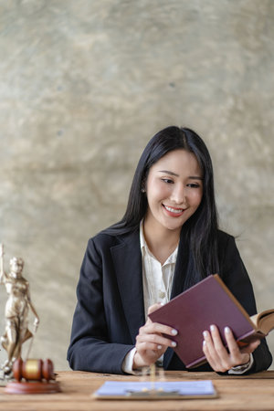 Attractive young Asian lawyer who works in the office with contracts and law books sits at a table...