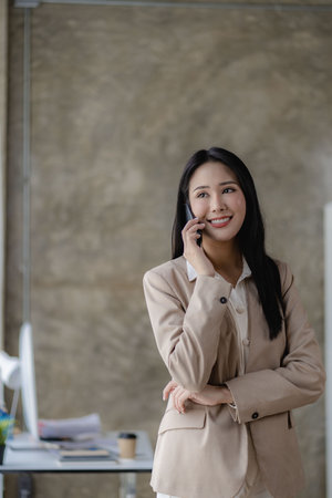Successful young Asian businesswoman smirking at her desk in the office vertical pictureの写真素材