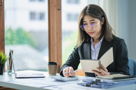 Asian business woman Use a laptop computer and work at the office with the calculator documents on the desk. plan to analyze financial reportsの写真素材