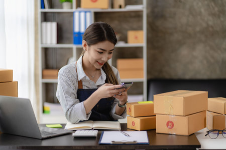 beautiful asian woman working at home selling online with yellow box and laptop on taking name orders from customers sme business concept parcel deliveryの写真素材