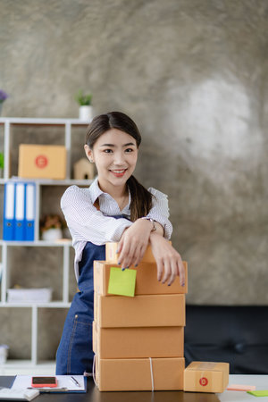 beautiful asian woman working at home selling online with yellow box and laptop on taking name orders from customers sme business concept parcel deliveryの写真素材