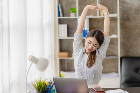 Asian accountant or female office worker stretching out her hand, relaxing at a desk at work.の写真素材