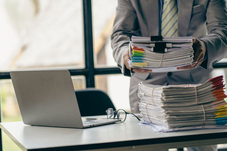 Businessman working in finance with pile of unfinished papers on the desk business paper pileの写真素材