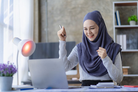 A Muslim business woman is very excited to close the sale. Arab woman smiling and working on laptop with financial chartの写真素材