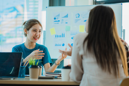Asian creative teams sit and work together to share inspirational creativity in a workshop. Young modern businessmen are meeting with graph paper and laptop in the workplace.の写真素材