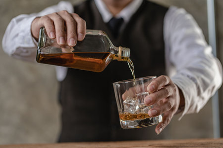 The bartender holds a glass of whiskey and ice to the male guest. The rest of the concept in the bar Close-up of serious businessman holding whiskey showing executive privilege conの写真素材